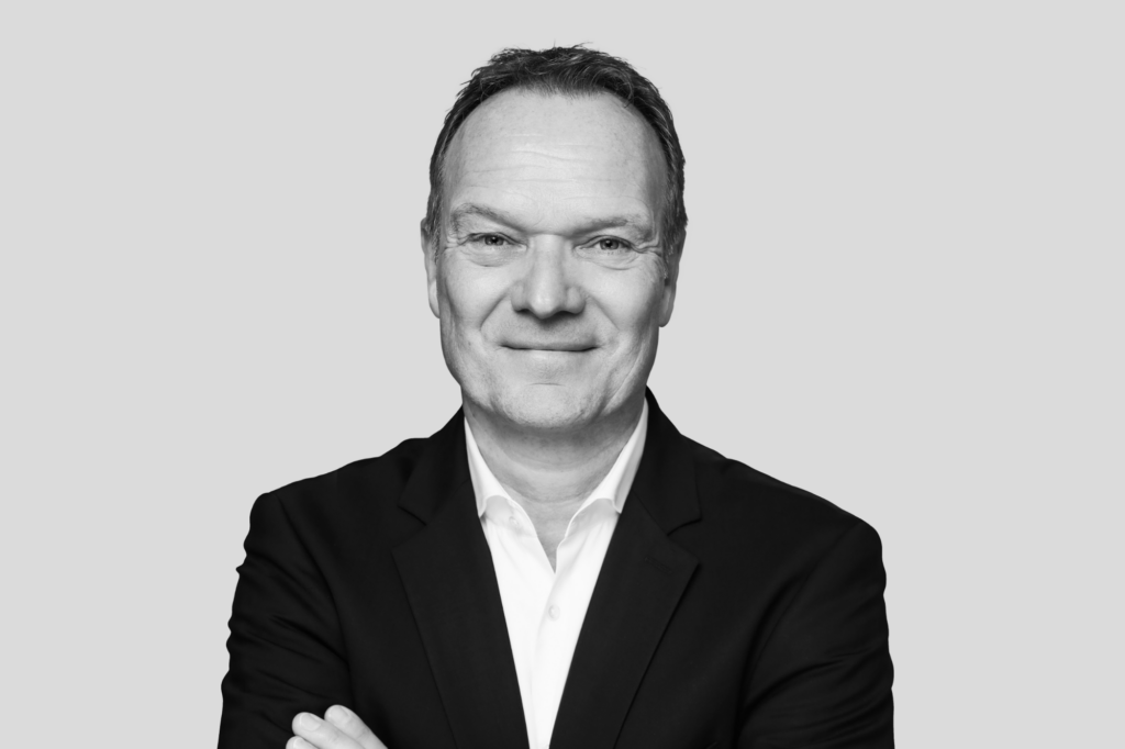 Schwarz-weiß Porträt eines Mannes im Anzug mit verschränkten Armen und freundlichem Blick.