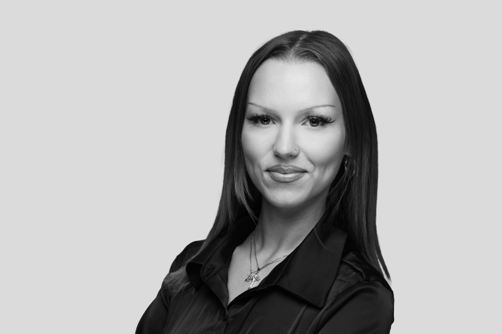 Schwarz-weiß Porträt einer Frau mit glatten Haaren und dunkler Bluse, die selbstbewusst in die Kamera blickt.