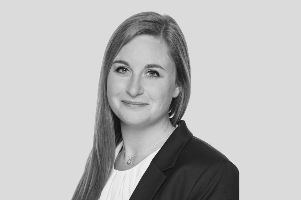 Porträt einer Frau mit langen Haaren, die in die Kamera blickt, in Businesskleidung vor hellem Hintergrund